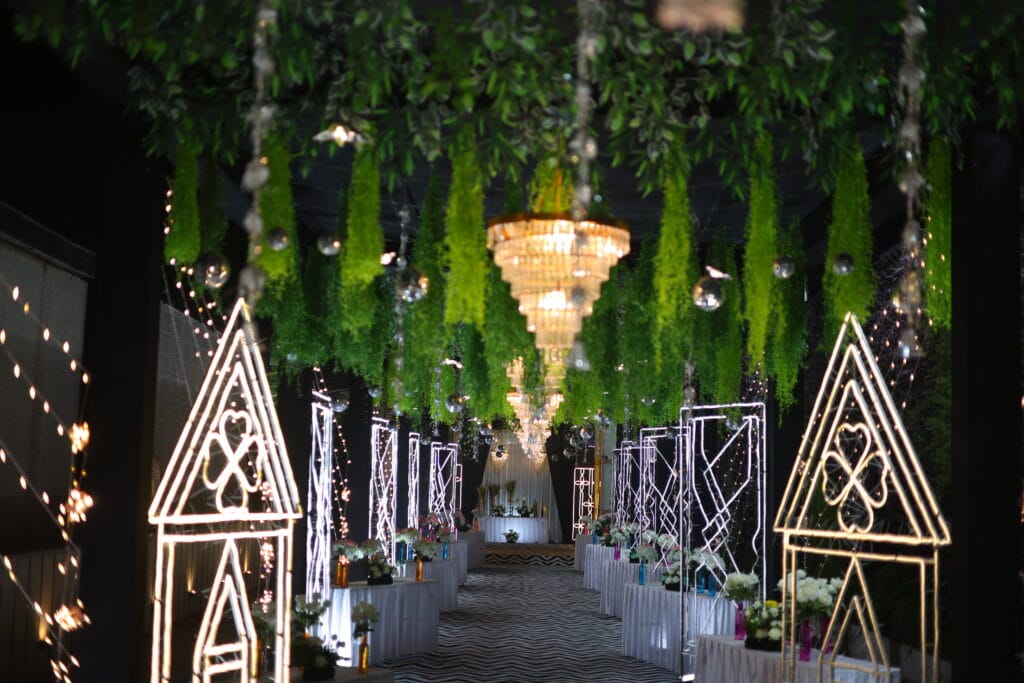 Modern wedding walkway with hanging green foliage, crystal chandeliers, and LED geometric frames designed by top Wedding Plannings in Jaipur